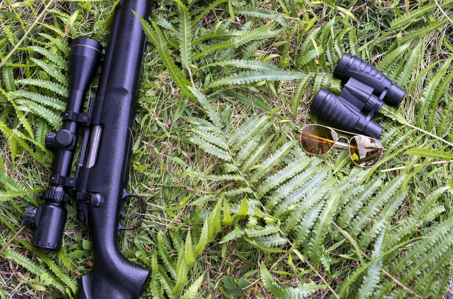 rifle de vista superior, binóculos e óculos de sol no chão de grama foto