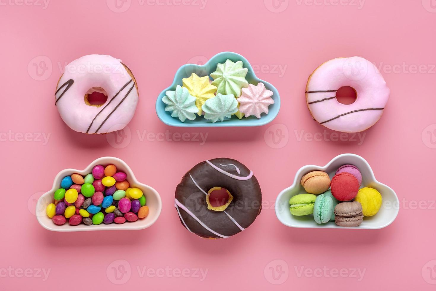 doces e merengues em tigela em forma de nuvem, chocolate com cobertura colorida e rosquinha rosa isolada em fundo rosa plana vista de cima knolling conceito de comida insalubre e saborosa foto