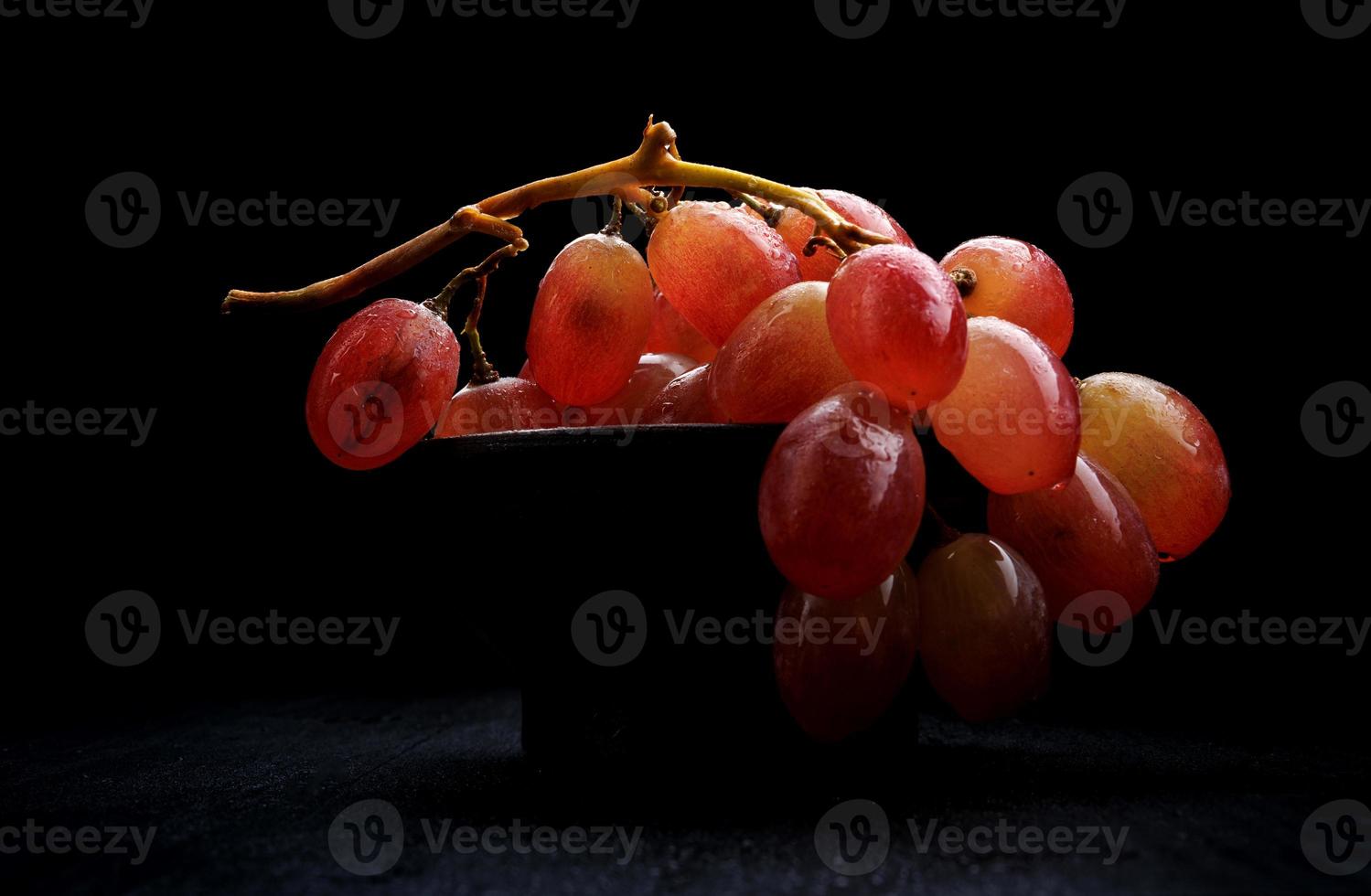 um cacho de uvas vermelhas maduras em um prato de barro, sobre um fundo escuro. foto