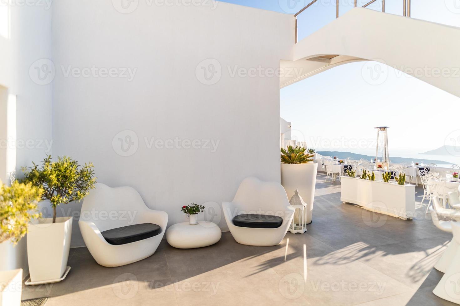 terraço branco no hotel de luxo, ilha de santorini. luxuoso restaurante e recepção do hotel. interior branco, cadeiras e mesa, céu azul suave e clima ensolarado foto