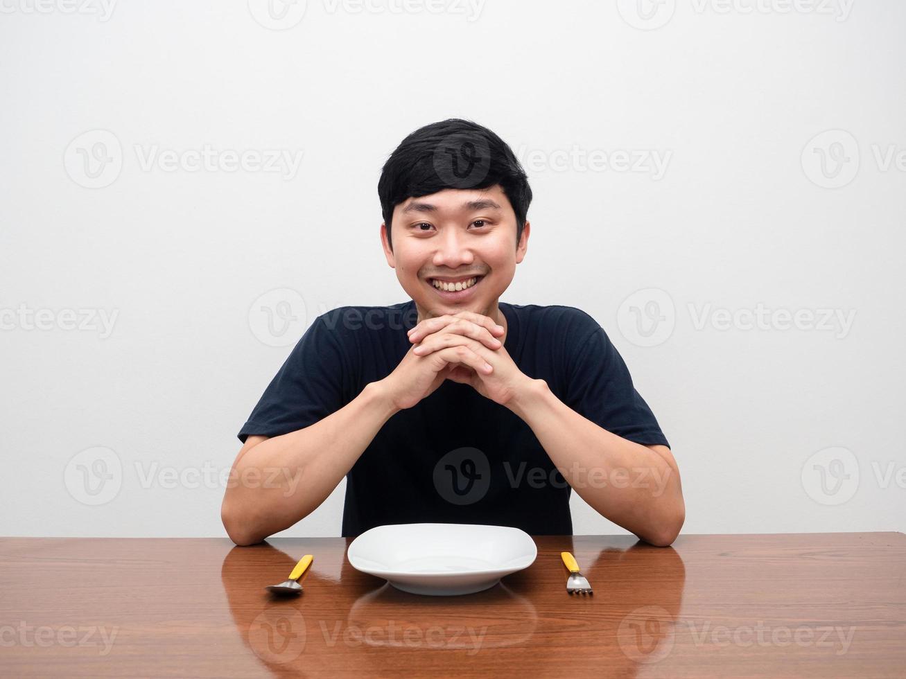 homem positivo sente-se pronto para jantar com o sorriso gentil, talheres de prato vazios na mesa foto
