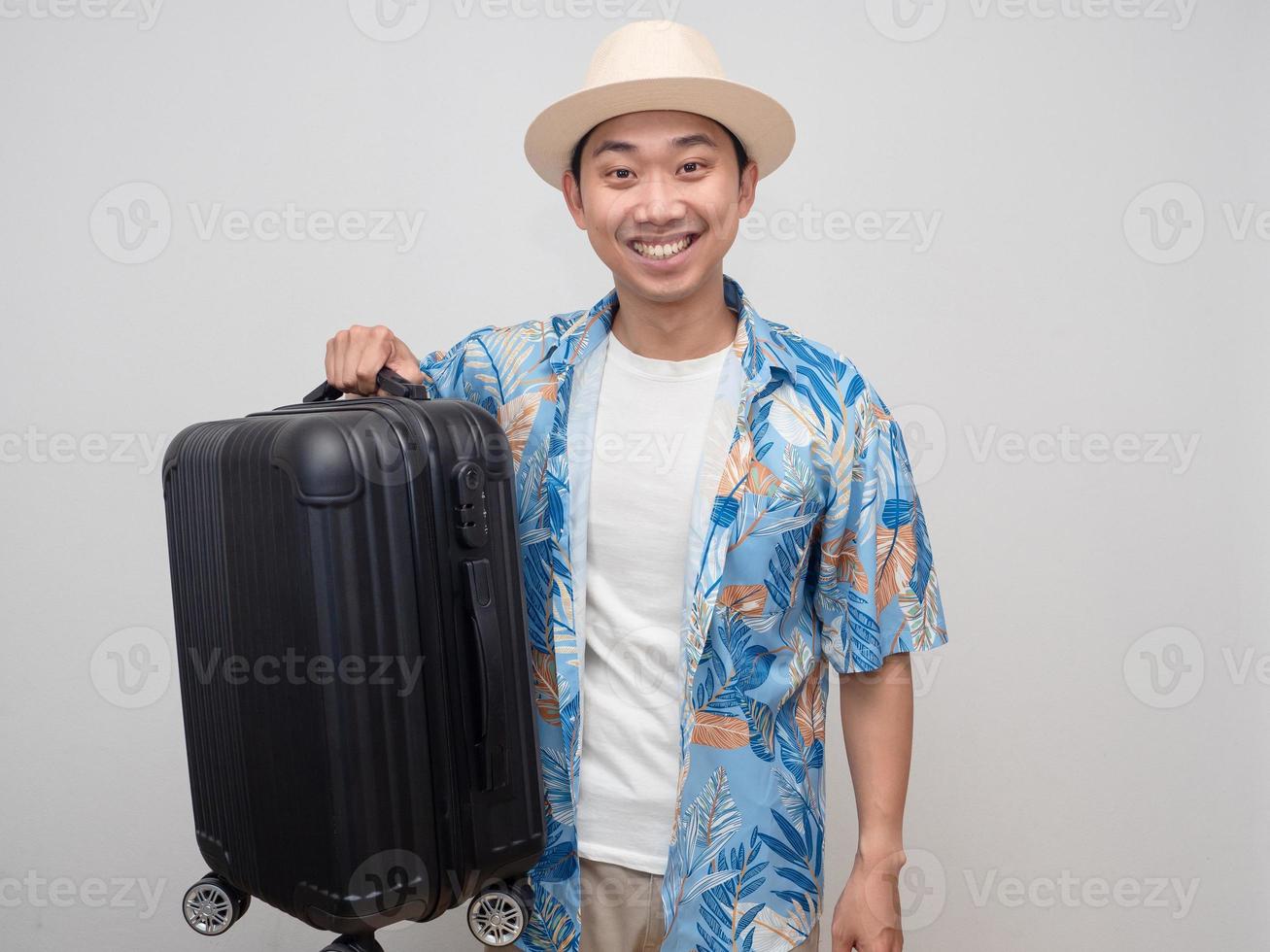 homem viajante positivo sorri feliz e mantém a bagagem isolada foto