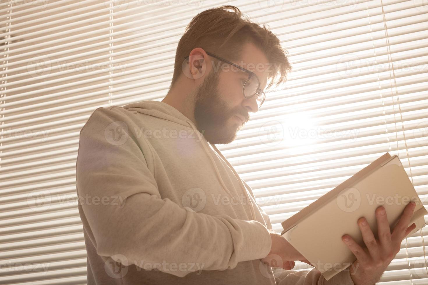 vista inferior do homem hipster elegante pensativo folheando seu planejador diário na frente das persianas. planejamento e conceito de economia de tempo foto