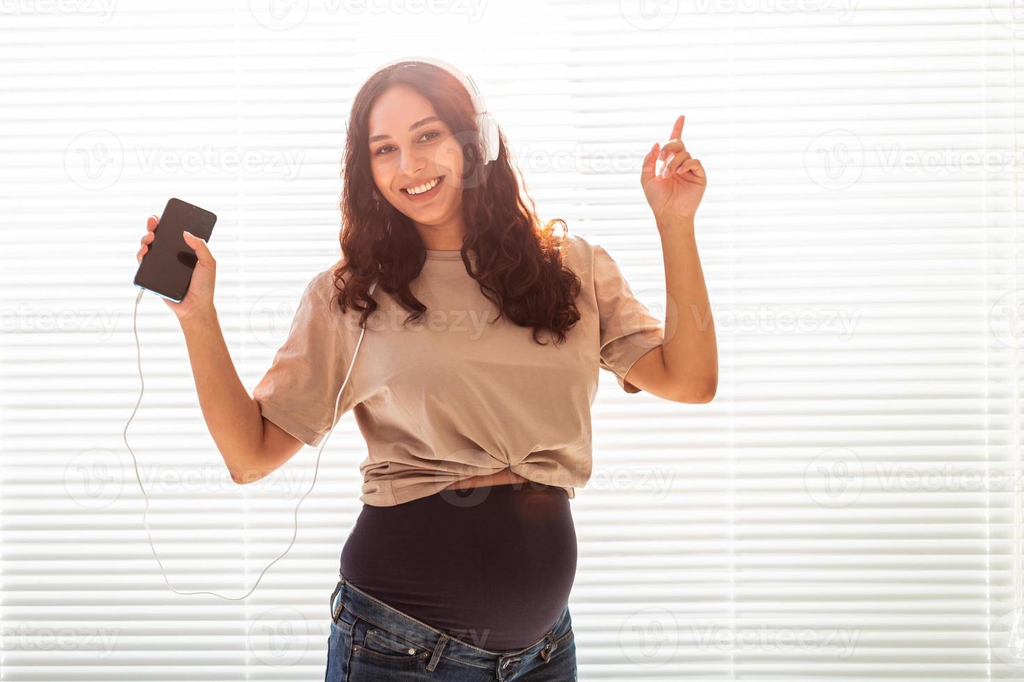 bela jovem pacífica grávida ouve música clássica agradável usando smartphone e fones de ouvido. conceito de atitude positiva antes do parto foto