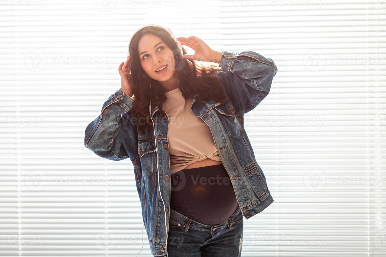 bela jovem pacífica grávida ouve música clássica agradável usando smartphone e fones de ouvido. conceito de atitude positiva antes do parto foto