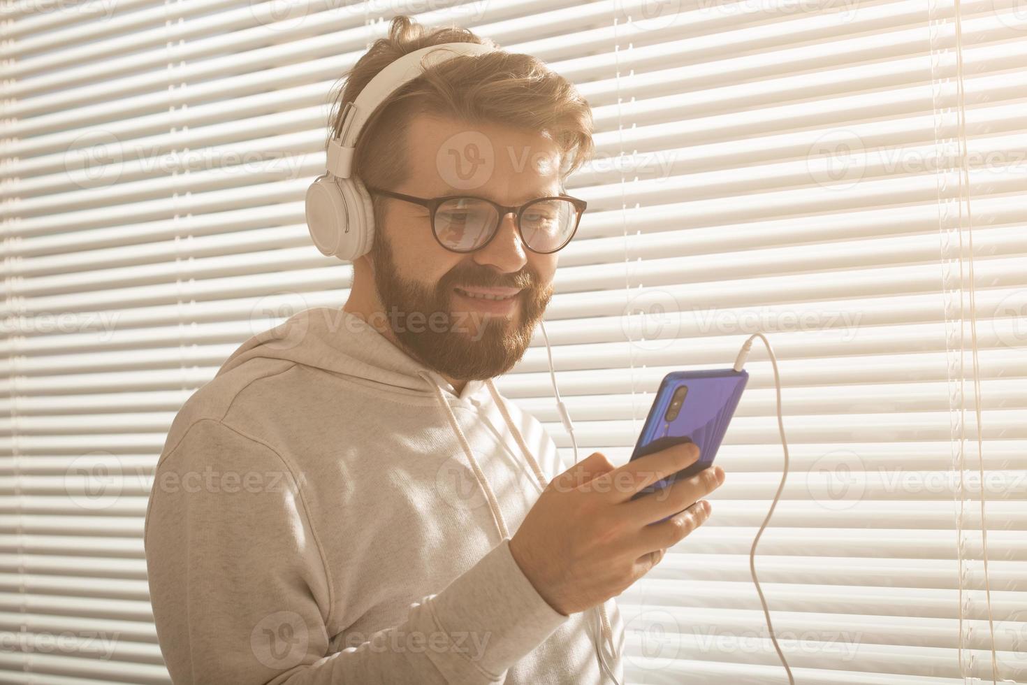 retrato de close-up do homem jovem elegante hipster escolhendo música favorita em smartphone com fones de ouvido no escritório. conceito de assinatura de música foto