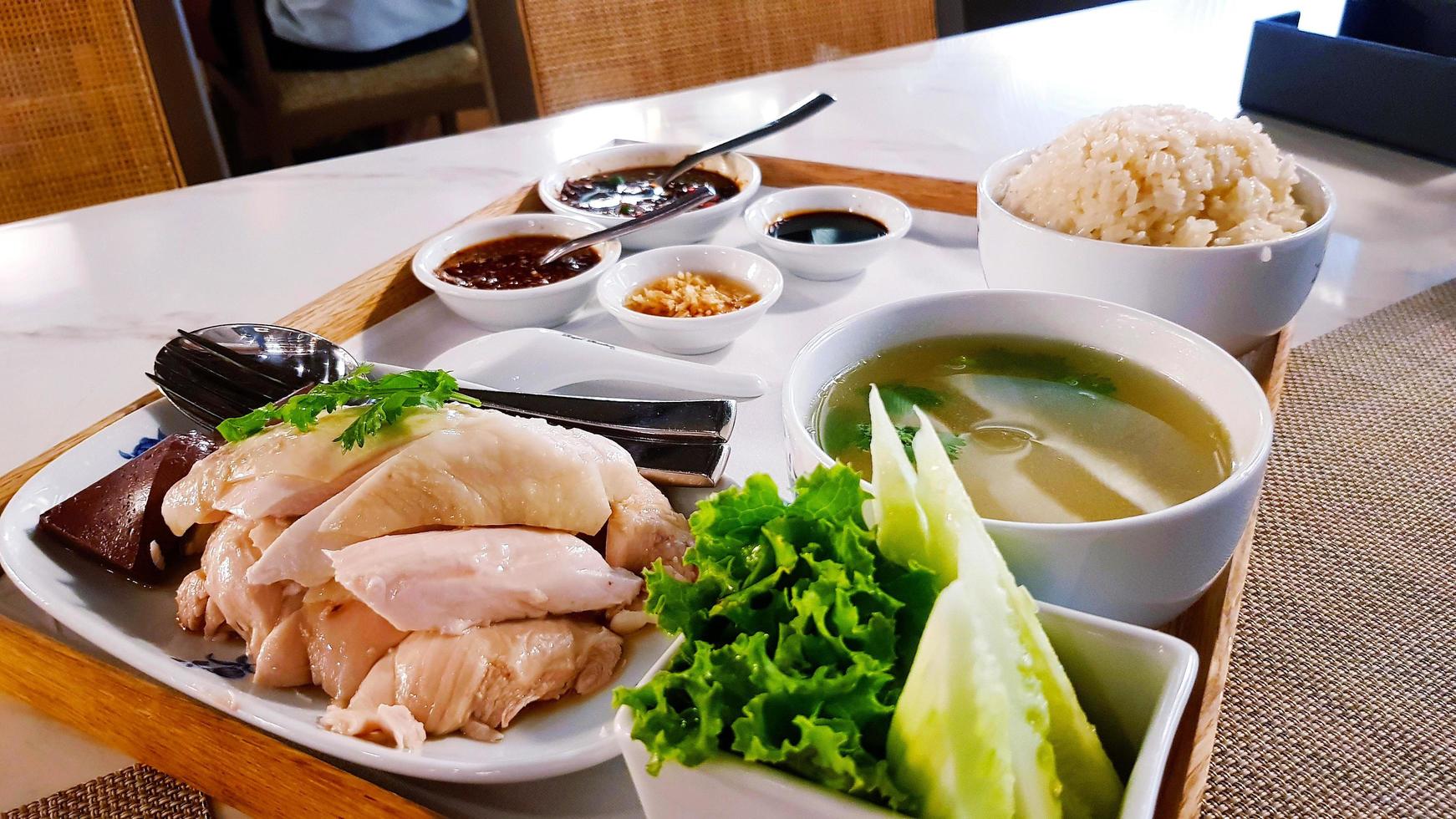 frango cozido com arroz cozido no vapor, sopa de pepino fresco, repolho verde, molho doce na bandeja de madeira. o povo tailandês chama essa comida de khao man gai. prato famoso na tailândia e no país de singapura. foto