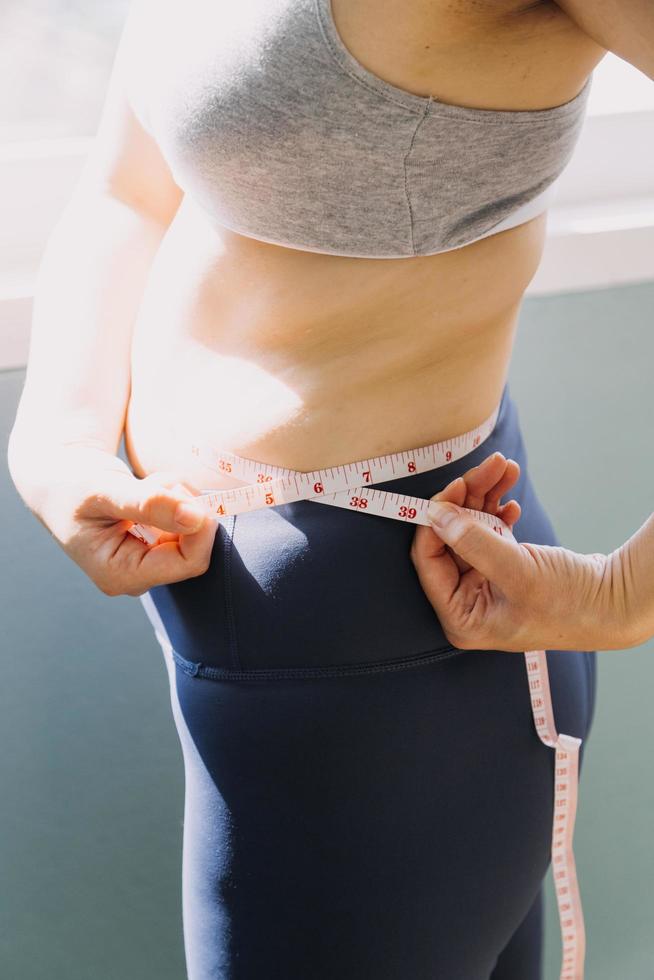 linda mulher gorda com fita métrica ela usa a mão para espremer o excesso de gordura que está isolado em um fundo branco. ela quer perder peso, o conceito de cirurgia e quebrar a gordura sob o foto