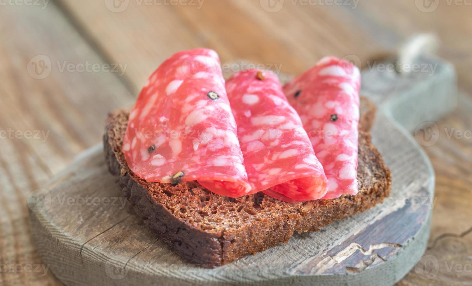 sanduíche com salame na tábua de madeira foto