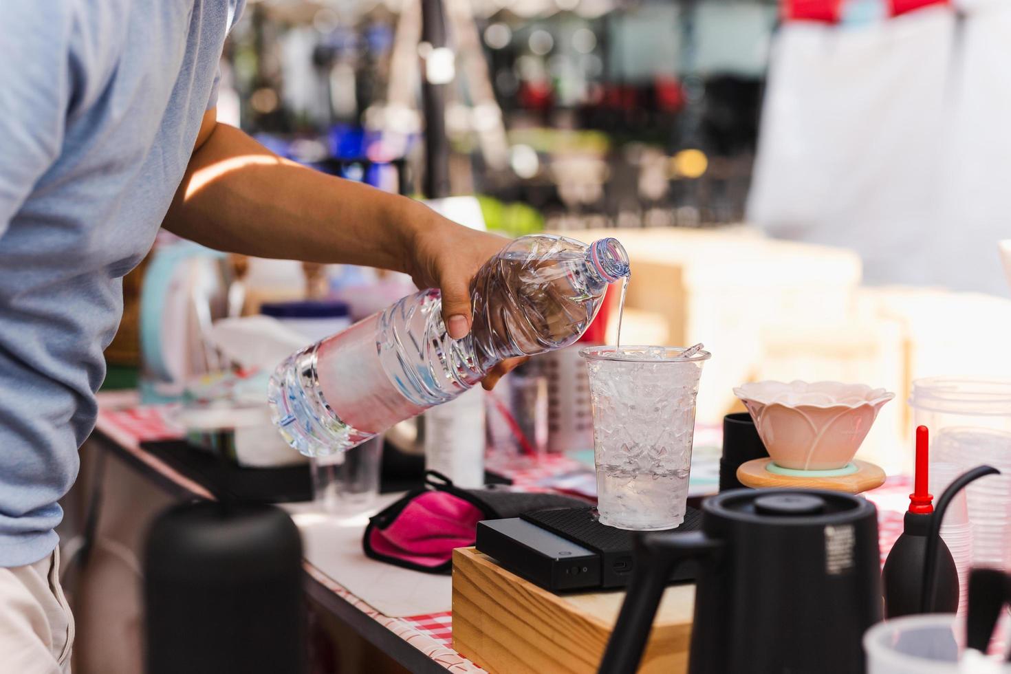 mão de barista despejando água em copo plástico com gelo. foto