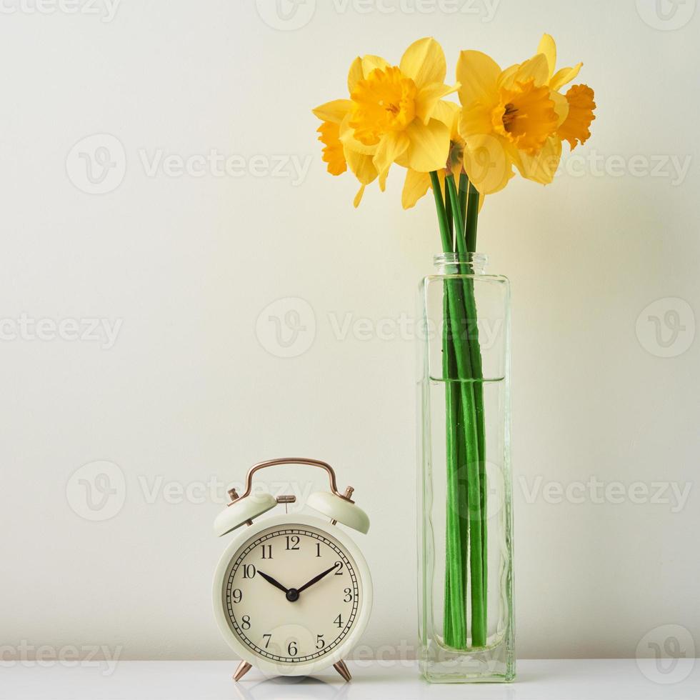 despertador e flores em vaso no fundo branco foto