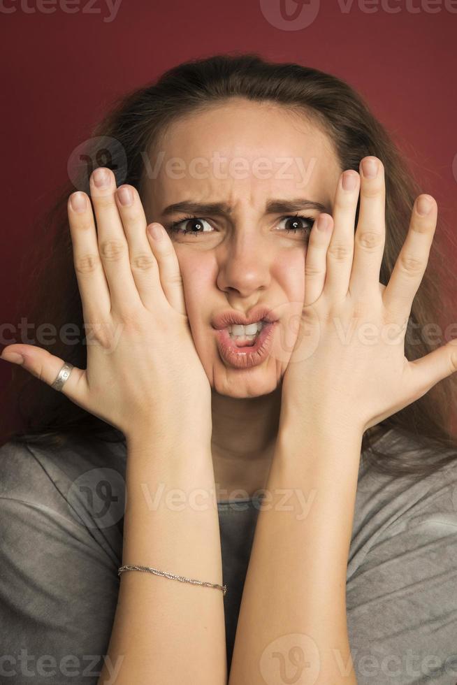 retrato de uma adolescente europeia emocional positiva usando seu cabelo claro em um coque, gritando de espanto ou espanto, mantendo as mãos no rosto foto