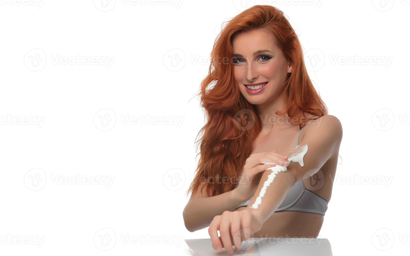 linda mulher de cabelo vermelho colocando loção corporal isolada no fundo branco foto