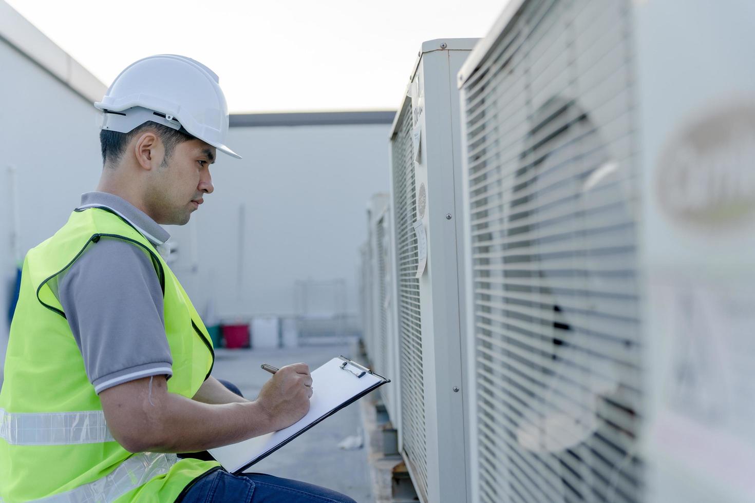 o engenheiro de manutenção asiático verifica novamente os trabalhos no telhado da fábrica. o empreiteiro inspeciona o sistema de compressor e planeja a instalação de sistemas de ar condicionado no canteiro de obras de edifícios modernos. foto