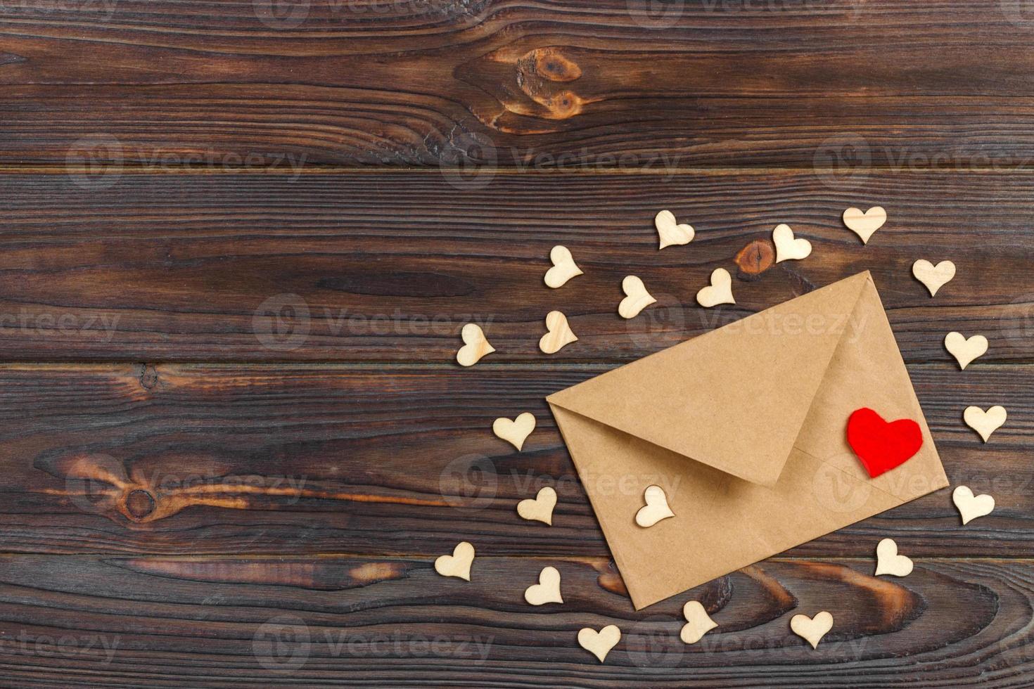 envelope e corações vermelhos de papel kraft marrom em fundo vintage envelhecido de madeira. saudação de dia dos namorados foto