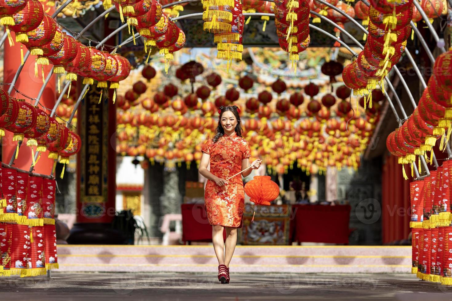 mulher asiática em vestido vermelho cheongsam qipao segurando lanterna enquanto visitava o templo budista chinês durante o ano novo lunar para o conceito de cultura tradicional foto