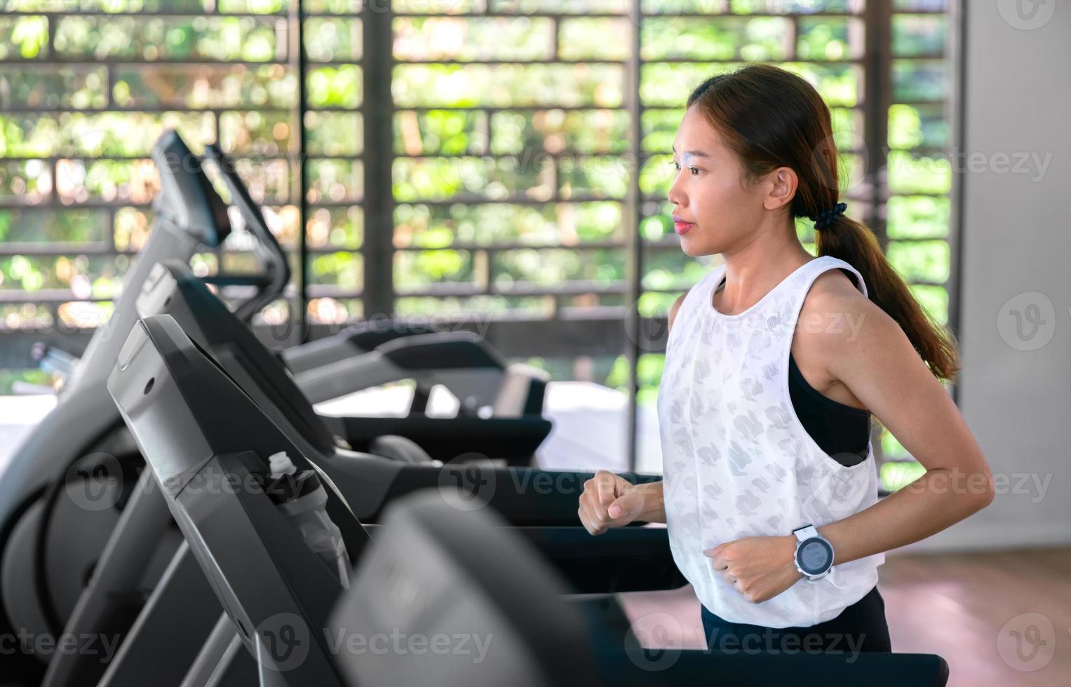 jovem atleta asiática feliz corre na esteira, máquina de corrida, no ginásio indoor fitness para a saúde foto