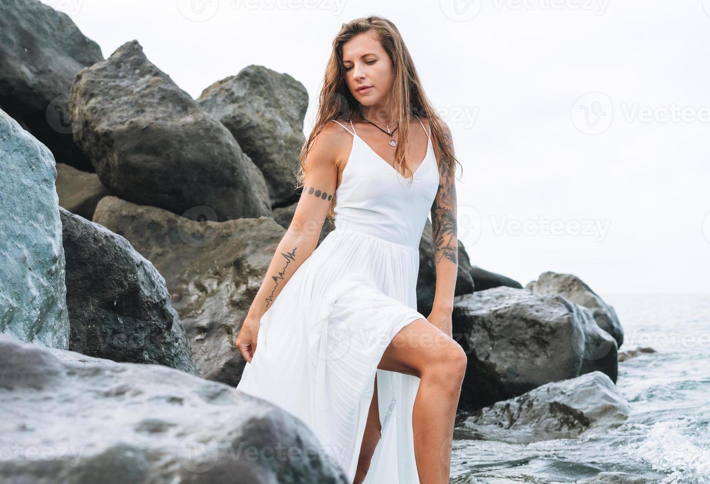 jovem mulher bonita despreocupada com cabelos longos em vestido branco curtindo a vida na praia do mar foto