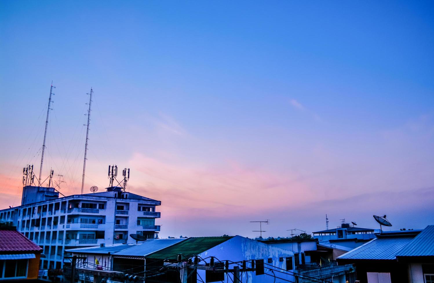 silhueta de edifícios na casa de vista do pôr do sol e torre de rádio de comunicação no céu roxo blackground foto