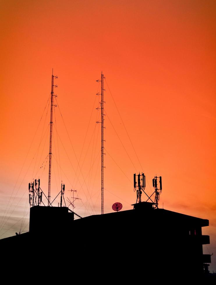 silhueta de edifícios na casa de vista do pôr do sol e torre de rádio de comunicação no céu laranja foto