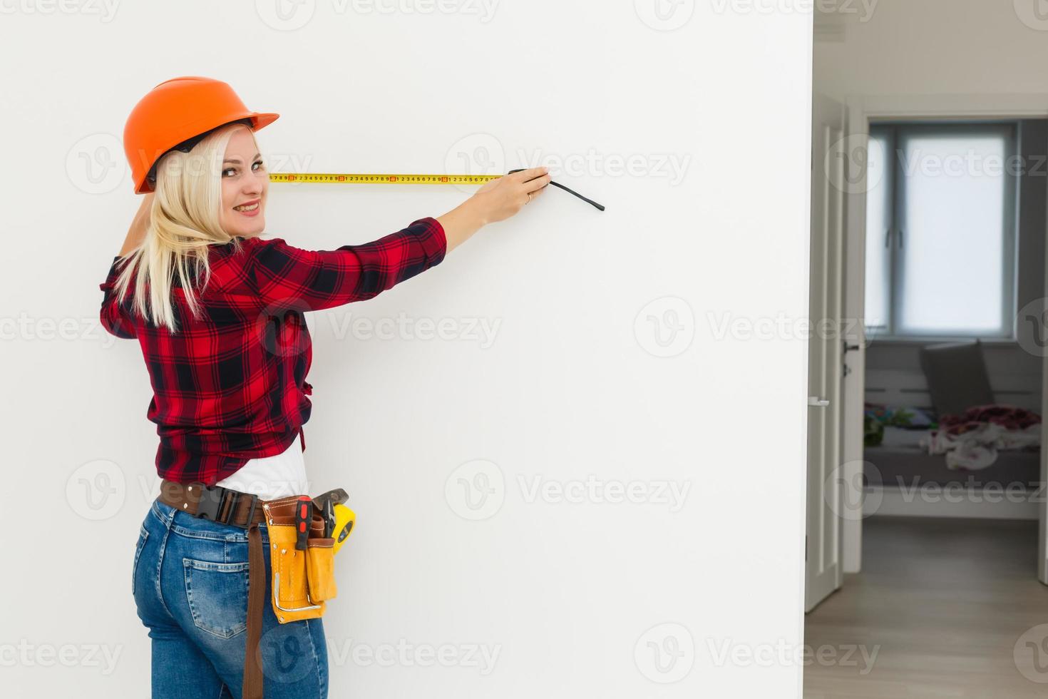 construtor de mulher de uniforme medindo parede com fita foto