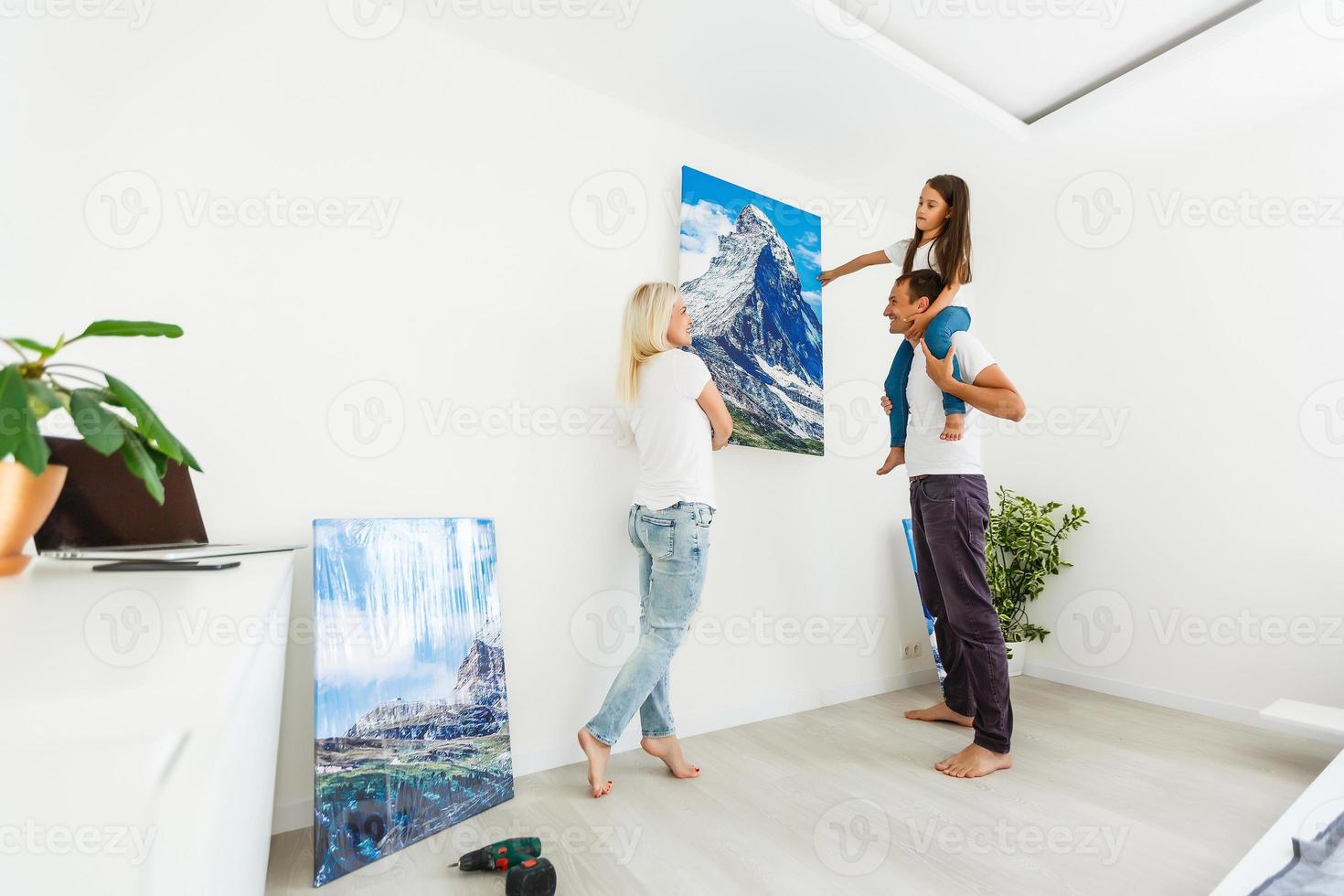 família pendura uma grande tela de fotos em casa