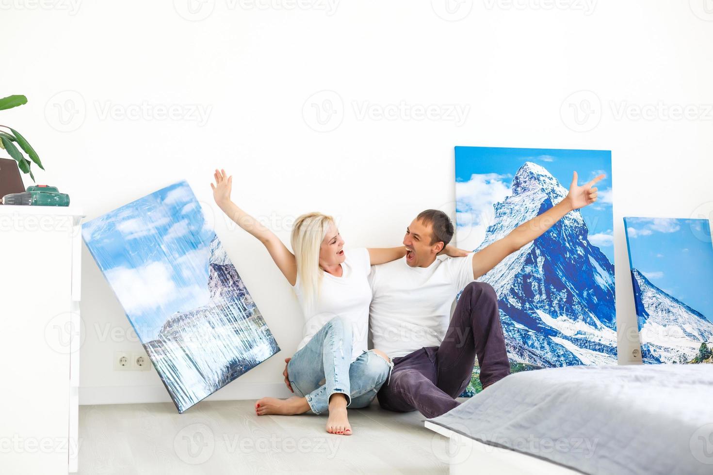 jovem casal pendura uma grande tela de fotos em casa