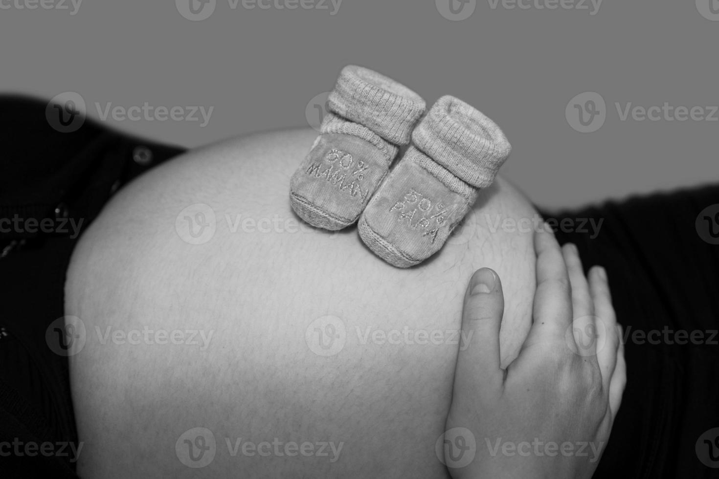 grávida com sapatinhos de bebê na barriga. mãe esperando o bebê recém-nascido foto