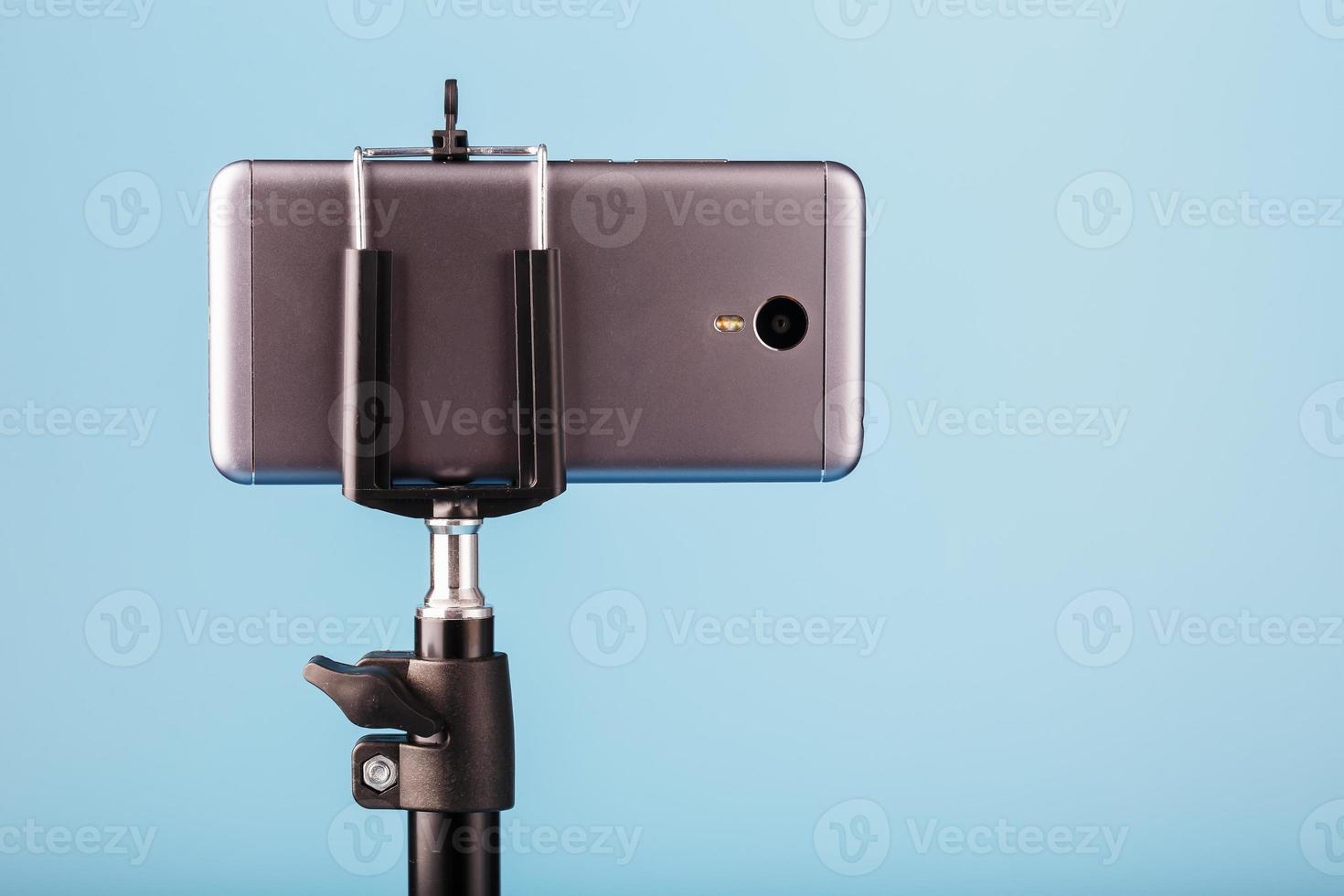 o smartphone é montado em um tripé como uma câmera de foto e vídeo para um blog em um fundo azul. gravar vídeos e fotos.