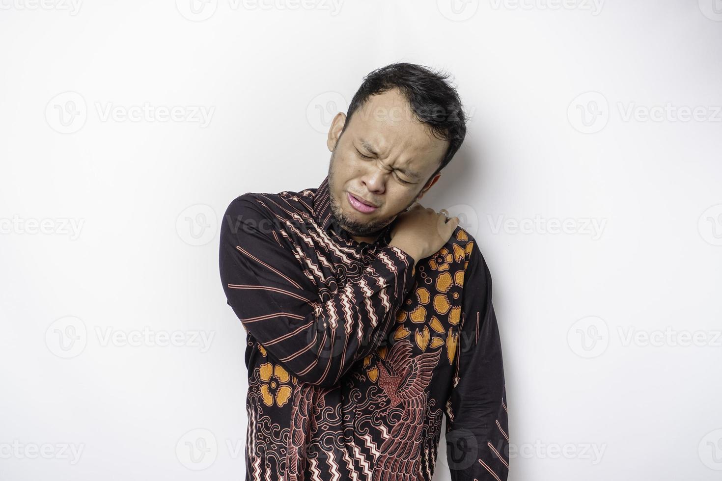 jovem chateado cansado usa camisa batik sofrendo de dor, espasmo muscular no local de trabalho. cansaço, prazo, dor e postura incorreta foto