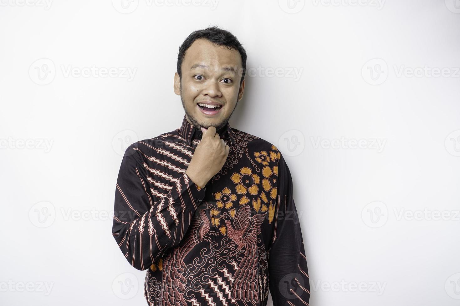 homem asiático pensativo vestindo camisa batik está olhando de lado enquanto toca seu queixo, isolado por fundo branco. foto