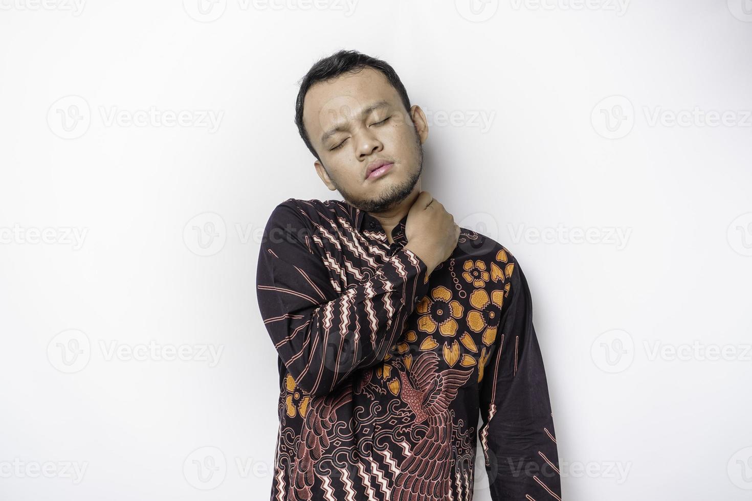 jovem chateado cansado usa camisa batik sofrendo de dor, espasmo muscular no local de trabalho. cansaço, prazo, dor e postura incorreta foto