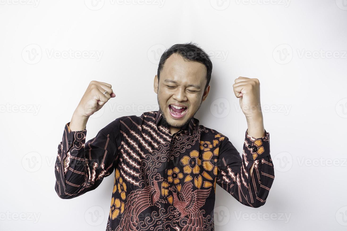 um jovem asiático com uma expressão feliz e bem-sucedida vestindo camisa batik isolada por fundo branco foto