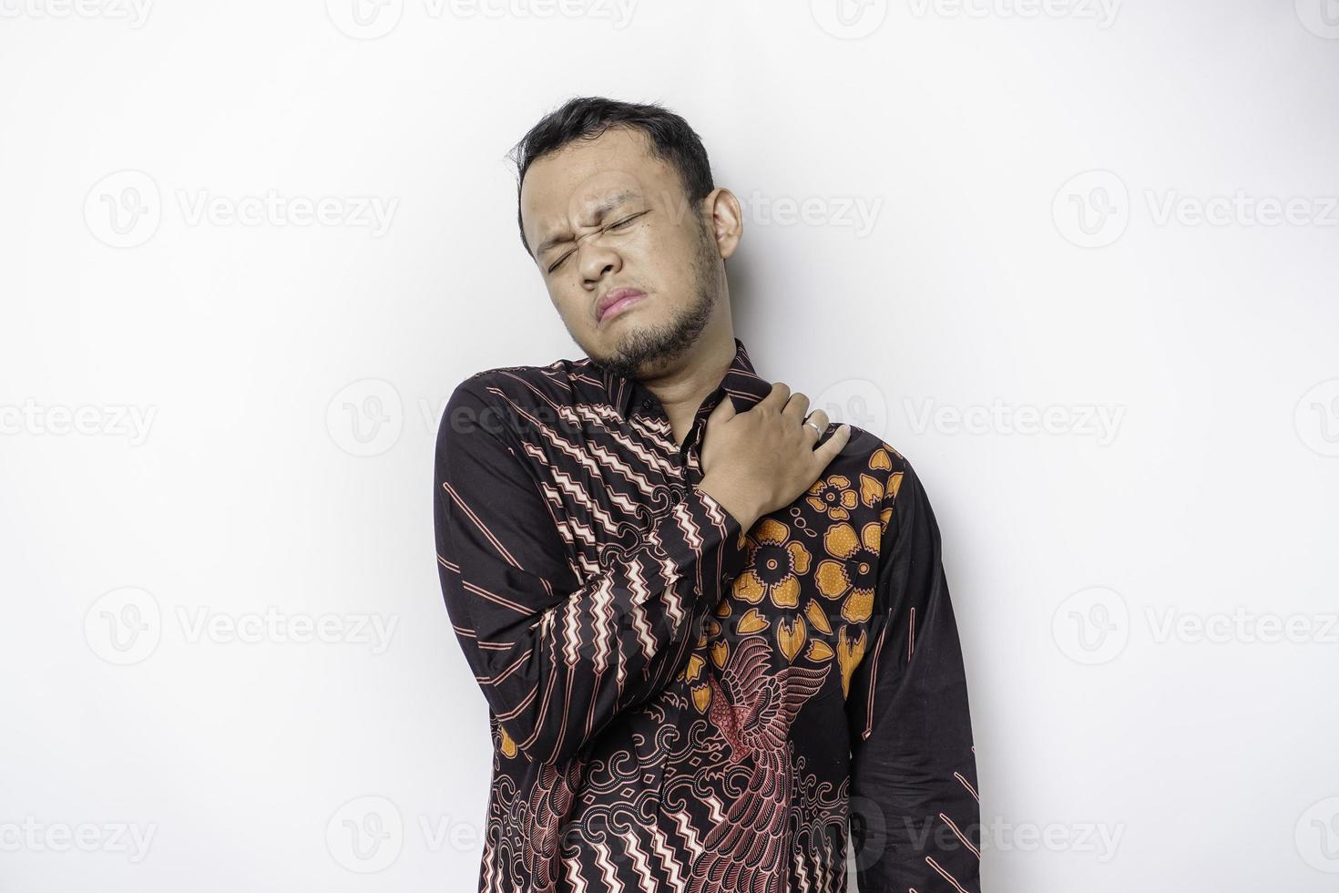 jovem chateado cansado usa camisa batik sofrendo de dor, espasmo muscular no local de trabalho. cansaço, prazo, dor e postura incorreta foto