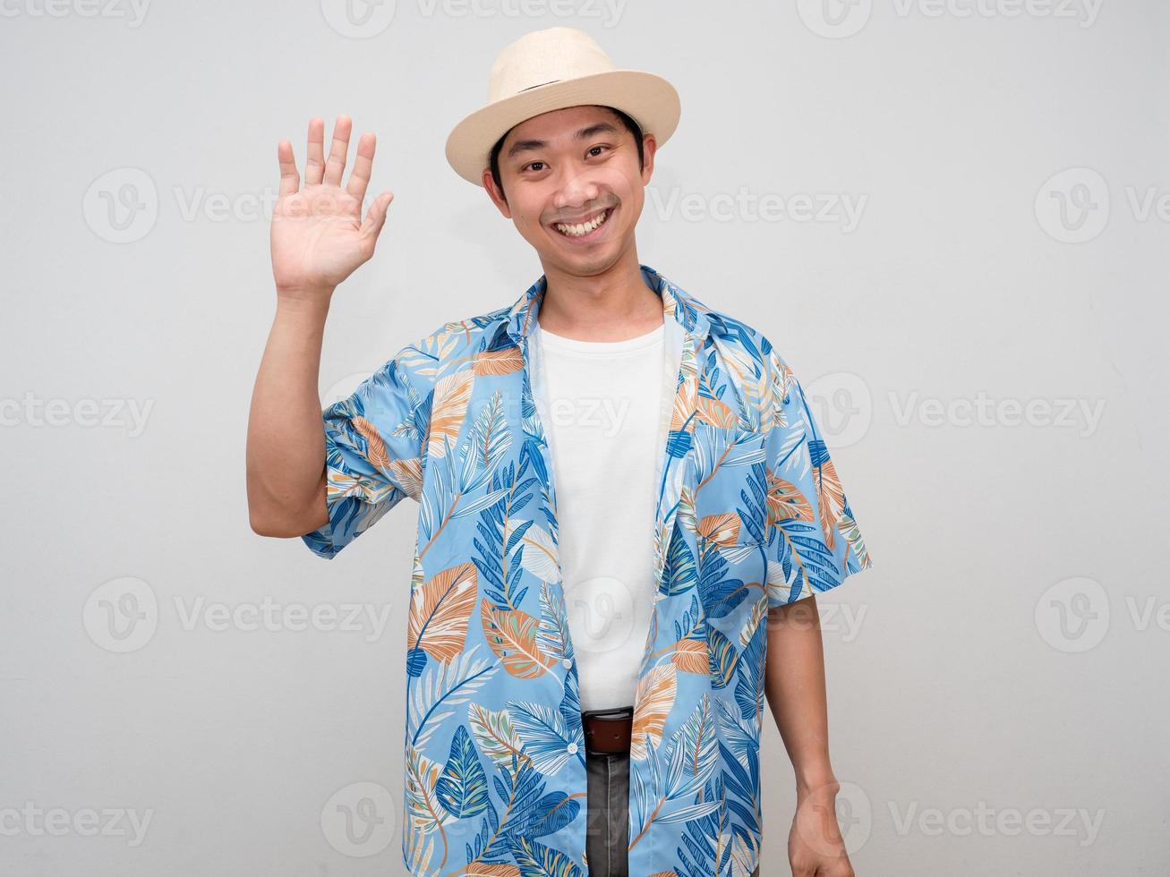 homem asiático positivo turismo camisa de férias usar chapéu sorriso feliz mostrar a mão para dizer olá isolado foto