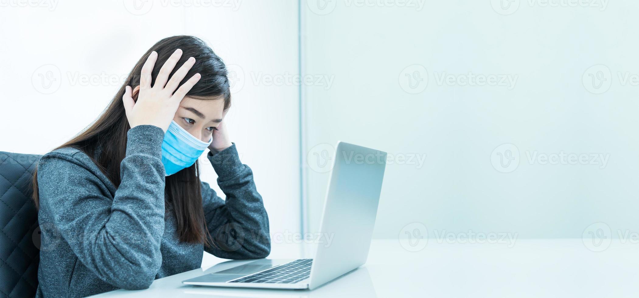 mulher usando laptop na mesa com dor de cabeça usando máscara para proteger covid-19 foto
