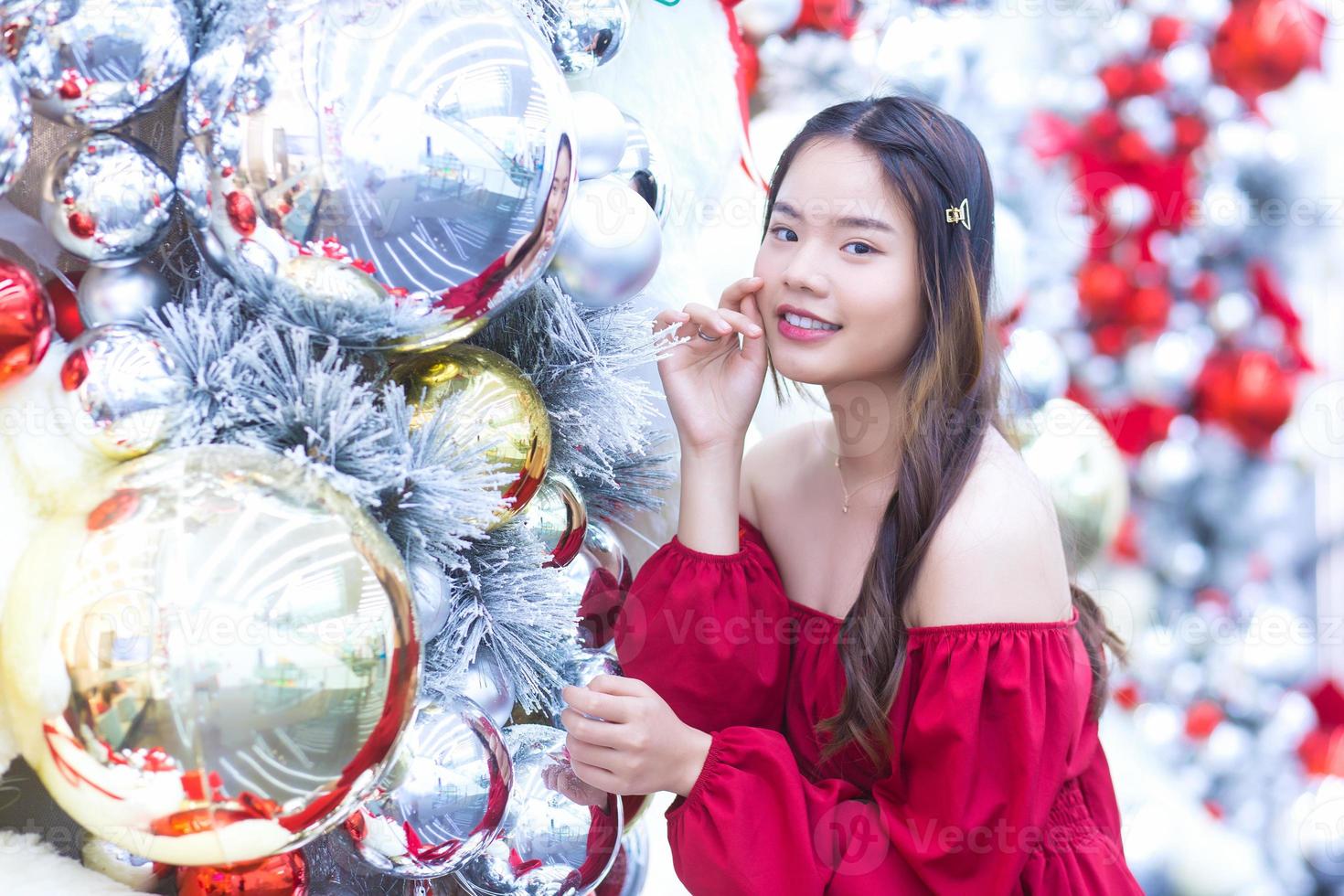 linda mulher asiática usa casaco vermelho enquanto olha para a câmera sorrindo alegremente no tema de celebração de natal e ano novo em bokeh de fundo. foto