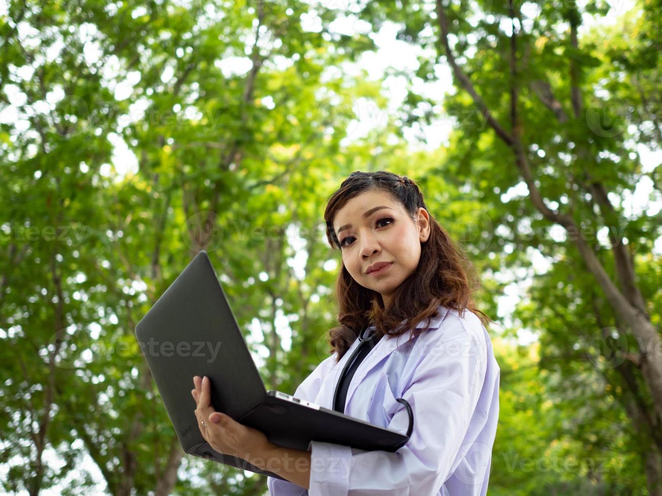 fêmea mulher senhora bonita bonita enfermeira médico cientista segurando notebook computador tablet olhando câmera ao ar livre jardim natural laboratório de pesquisa médico ciência cuidados de saúde médico foto