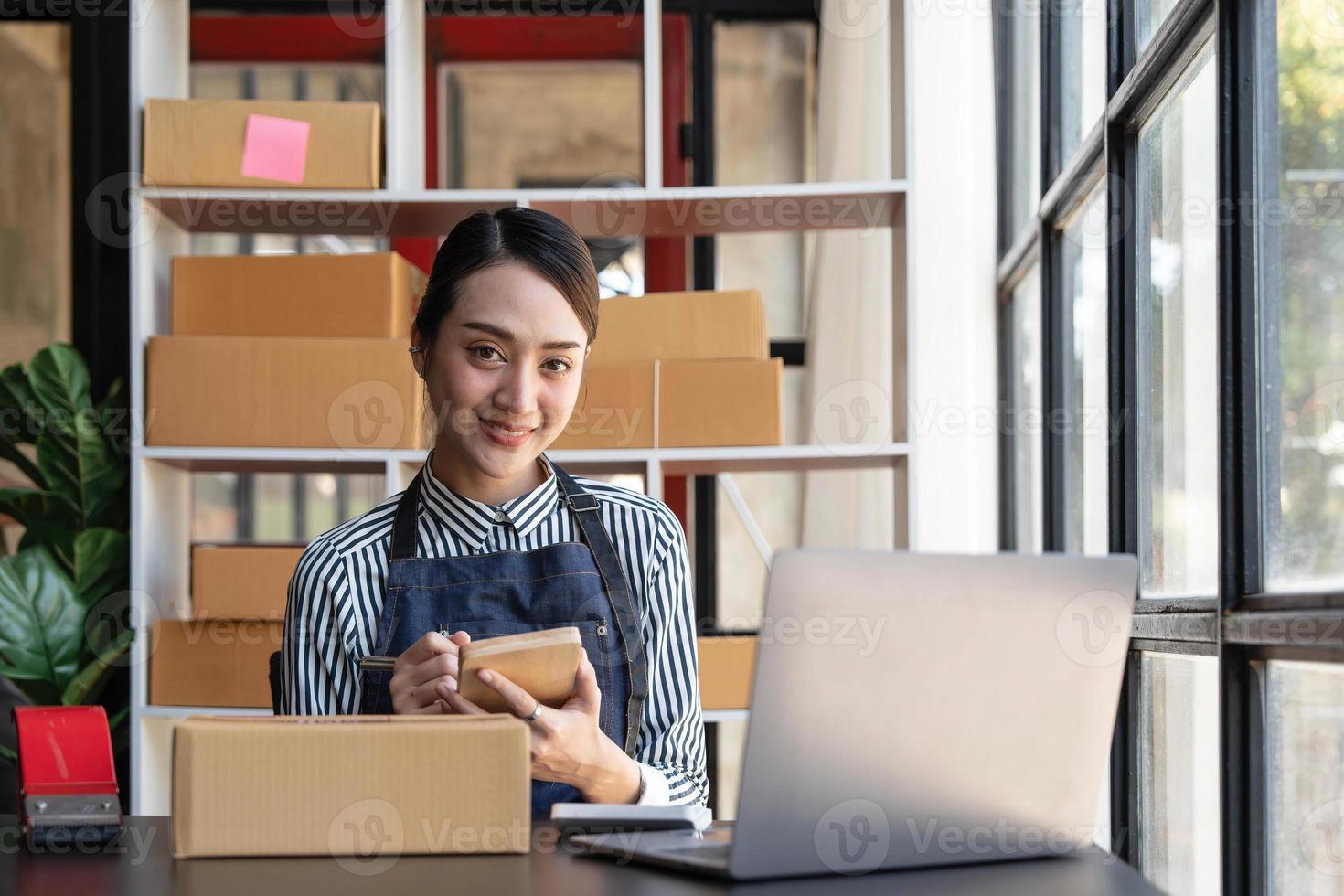 iniciando uma pequena empresária proprietária de uma pequena empresa, lendo e escrevendo números de pedidos. receber e revisar pedidos on-line para se preparar para embalar caixas, vender para clientes, ideias de negócios para pequenas e médias empresas on-line. foto