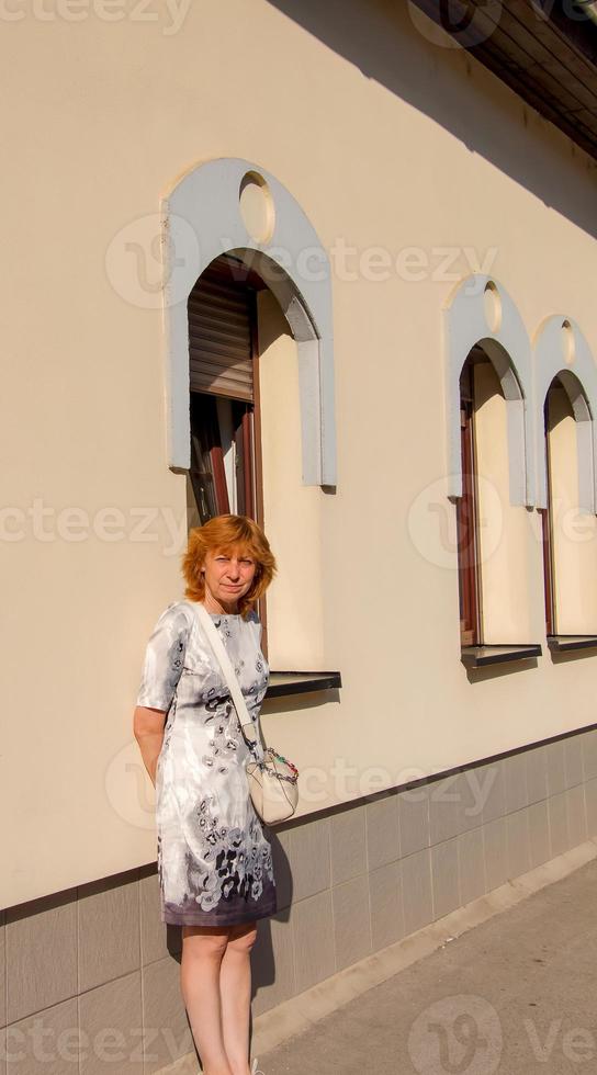 uma mulher madura de meia-idade com cabelos loiros caminha pelas ruas de uma cidade europeia. foto