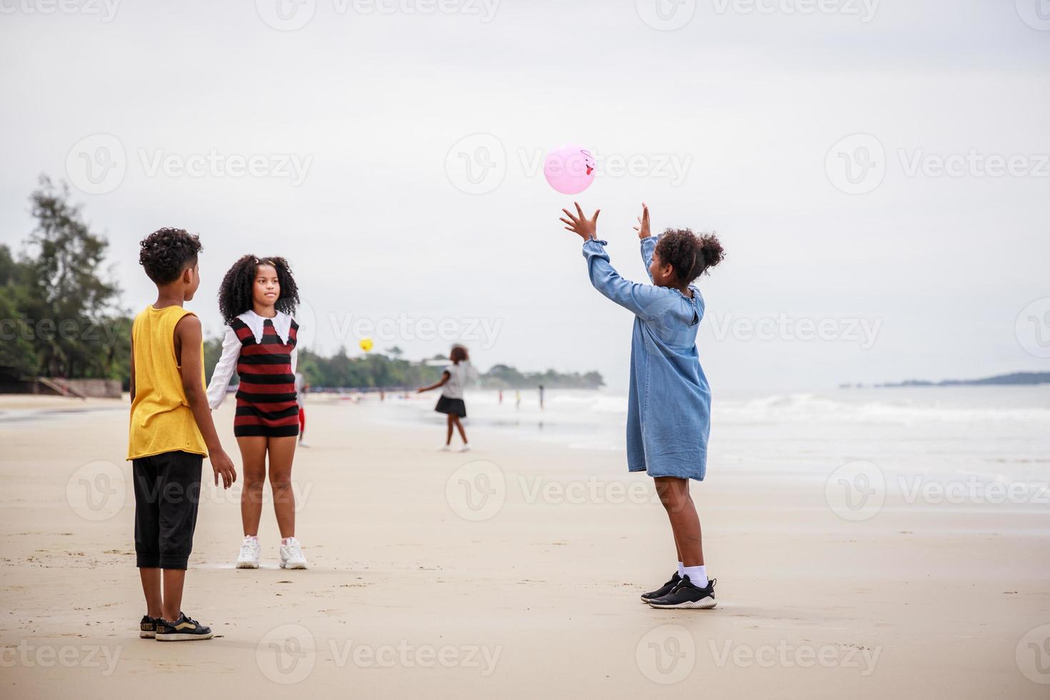feliz de um grupo de crianças afro-americanas jogando bola de praia na praia contra o céu claro foto