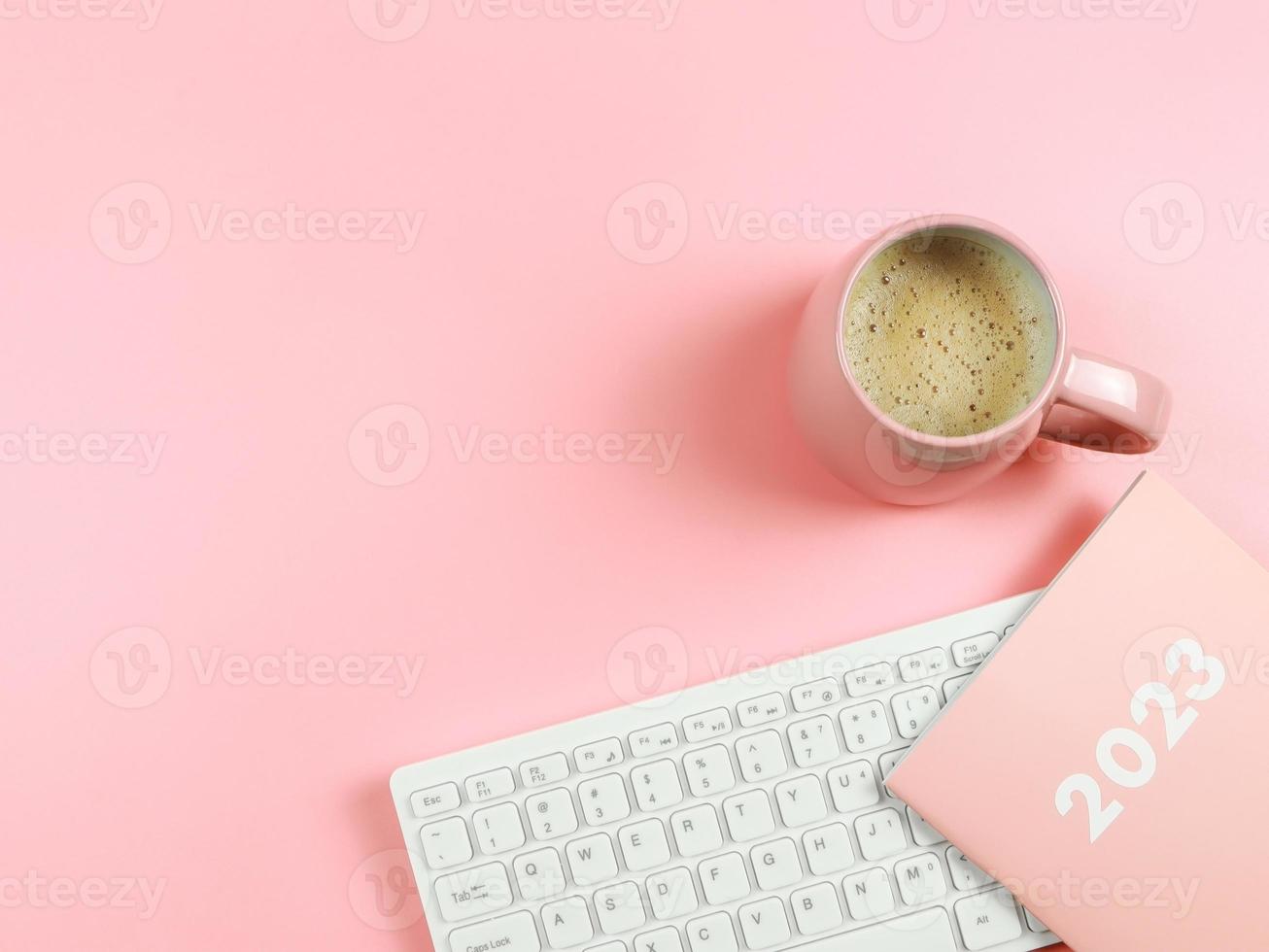 configuração plana de teclado de computador, diário rosa de xícara de café rosa ou planejador 2023 em fundo rosa com espaço de cópia. foto