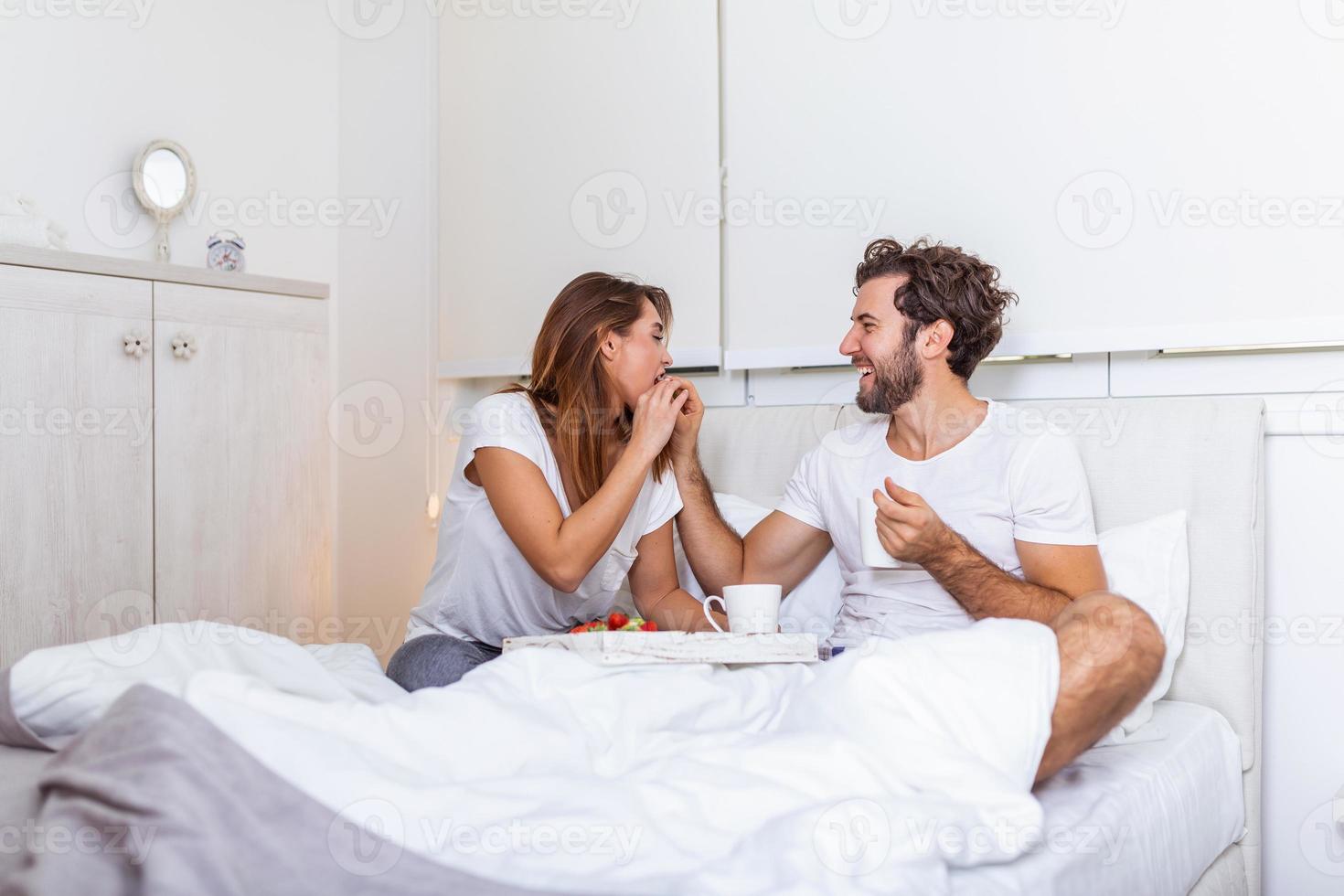 jovem bonito alimentando jovem atraente na cama pela manhã. café da manhã romântico para dois. amor, cuidado, relacionamentos. casal tomando café da manhã saudável juntos na cama em casa foto