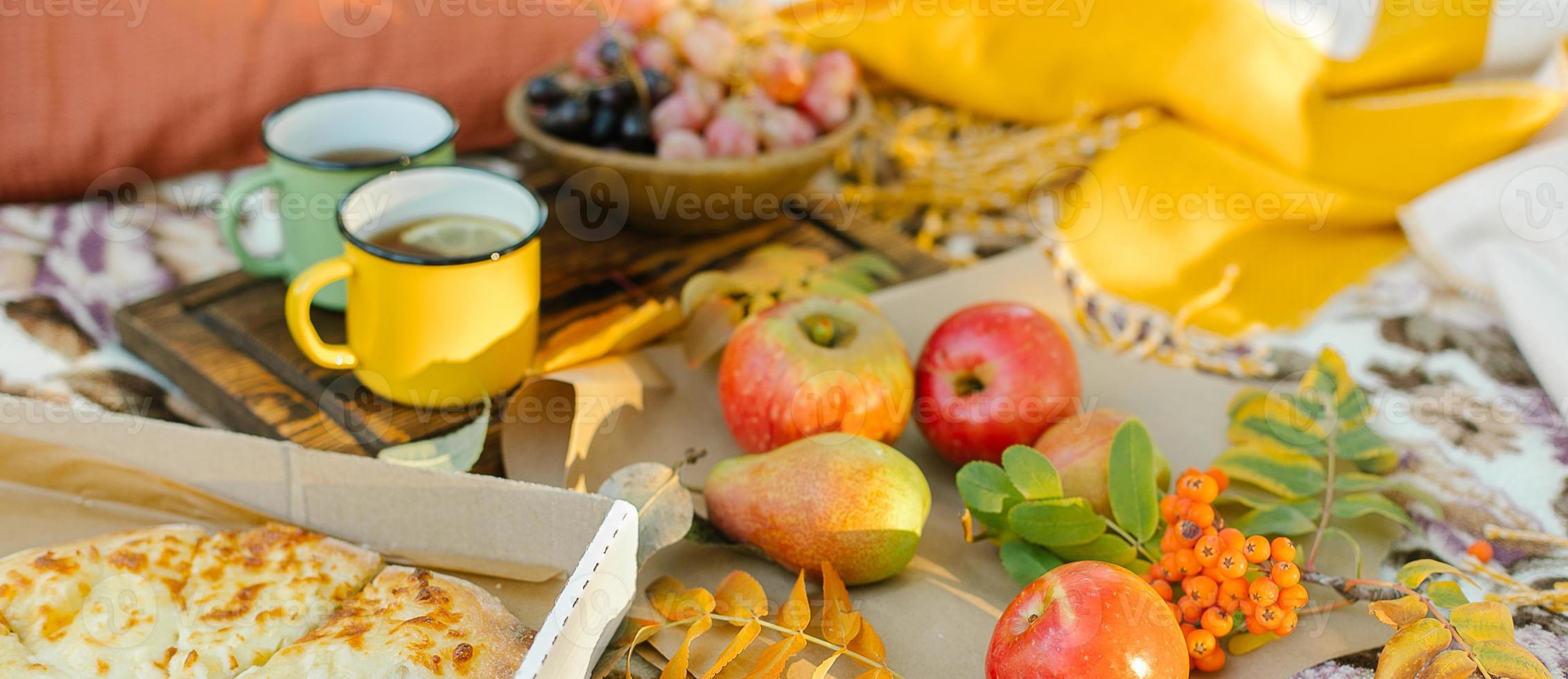 xícaras de chá, frutas e uvas em xadrez no parque. piquenique de outono na natureza. conceito ao ar livre de outono aconchegante. foto