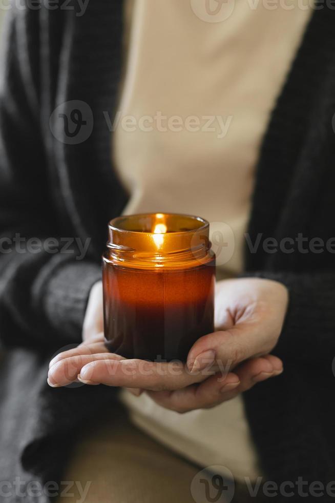 mulher segurando na mão uma vela acesa em uma pequena jarra de vidro âmbar com pavio de madeira. zen e relaxe o conceito. foto