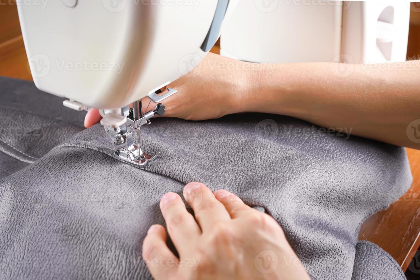 mãos femininas costurando tecido cinza na máquina de costura moderna. close-up vista do processo de costura. foto