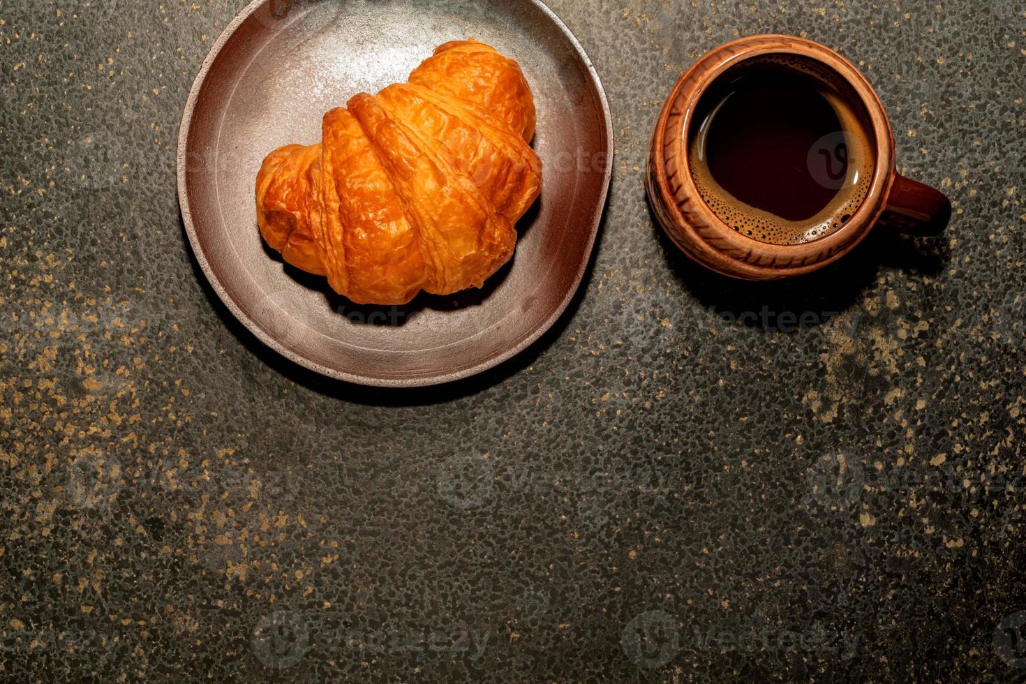 croissant de café da manhã no prato e café na mesa de pedra. foto