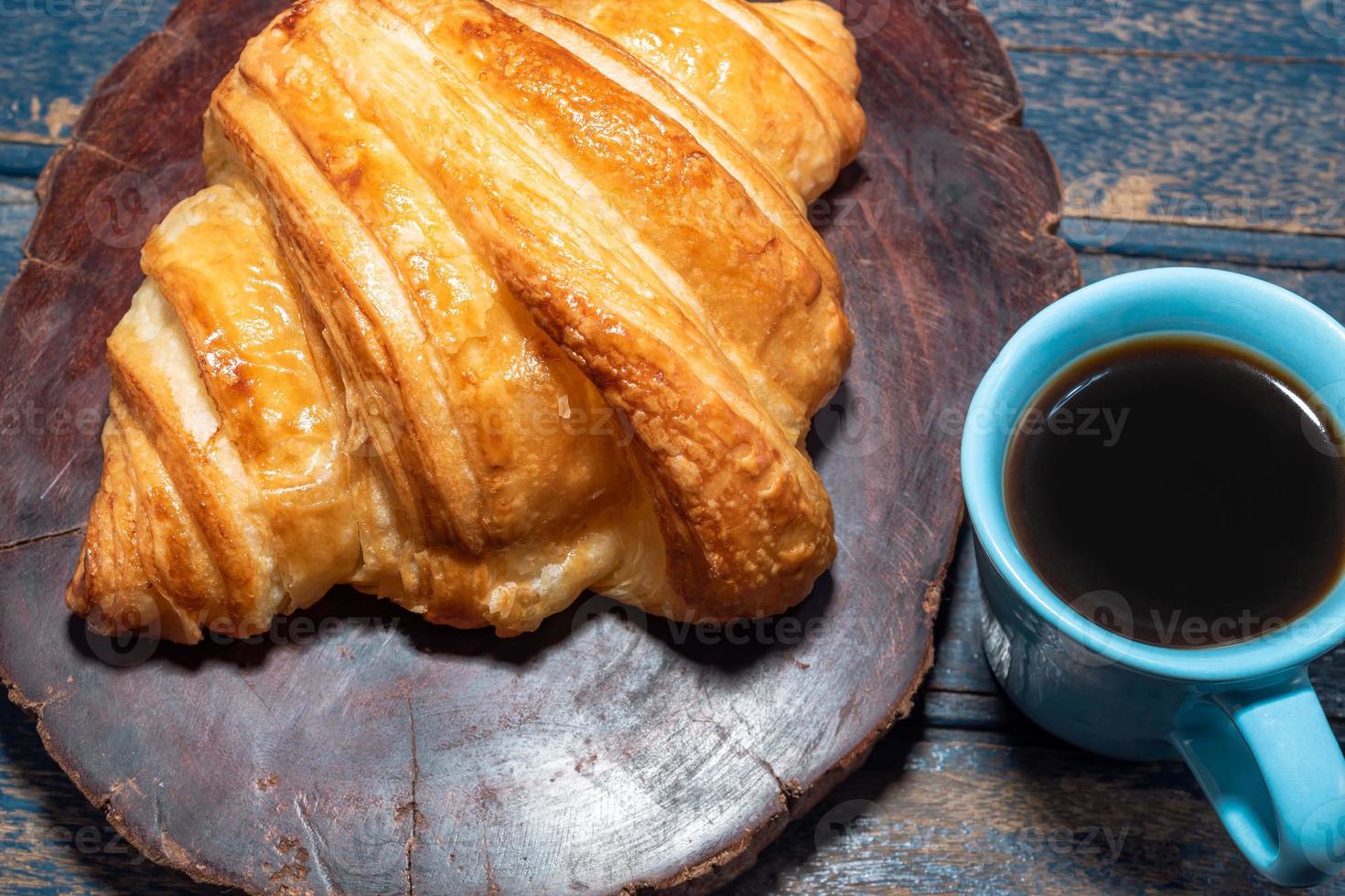 croissant de café da manhã no prato e café na mesa de madeira. foto