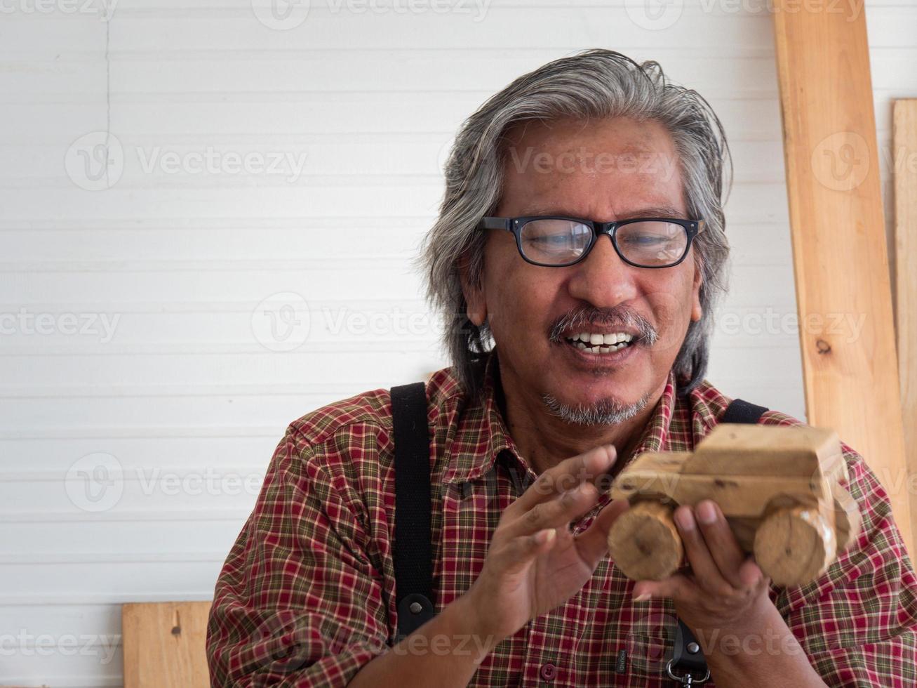 feliz homem sênior asiático está curtindo seu hobby pintando diligentemente casas de pássaros na oficina. foto