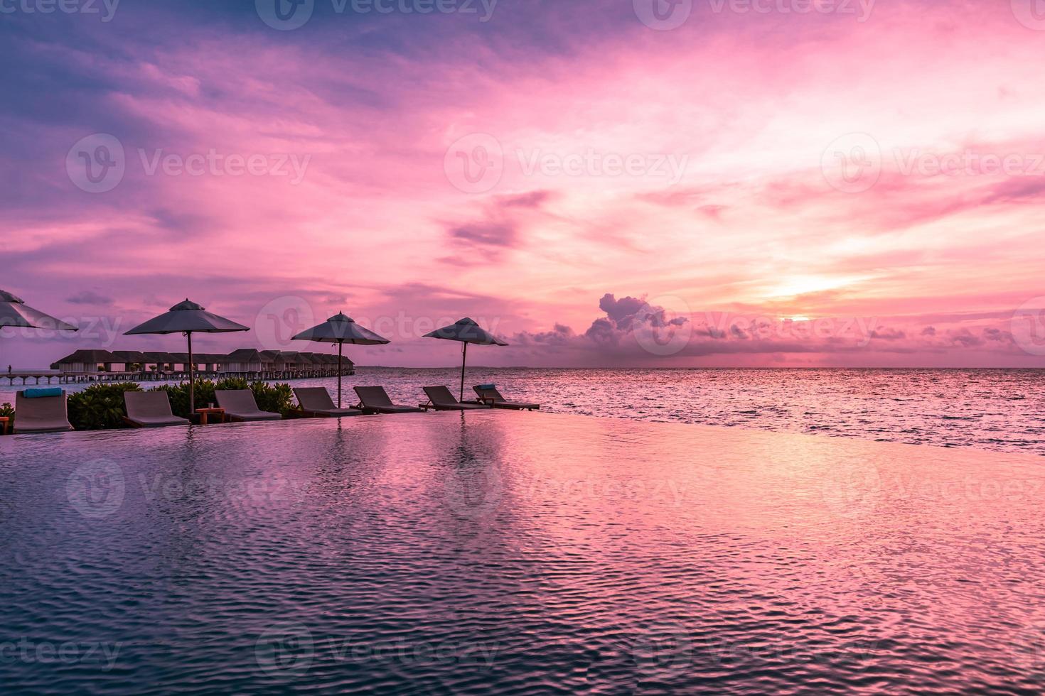 guarda-chuva e cadeira ao redor da piscina infinita perto da praia do oceano ao nascer ou pôr do sol. para viagens de lazer e conceito de férias, paisagem de resort de verão. férias de relaxamento tropical, pôr do sol foto